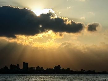 Silhouette city by sea against sky during sunset