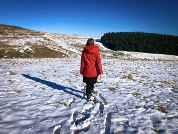 Rear view of woman in red coat walking on a field covered in snow