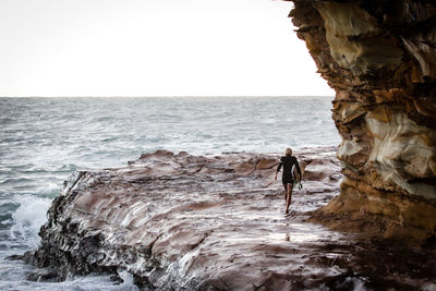 Man standing on cliff by sea against clear sky