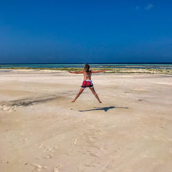 Rear view of woman jumping at beach against sky