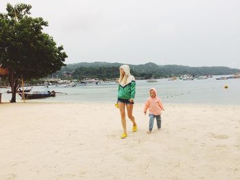 Full length of girl walking with mother on beach against sky