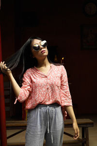 Beautiful young woman wearing sunglasses standing at home