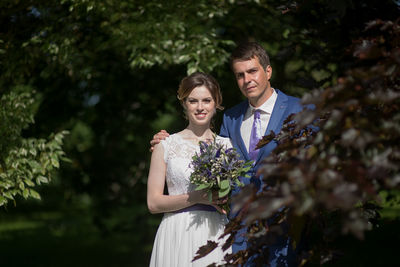 Portrait of bride with bridegroom holding bouquet at park