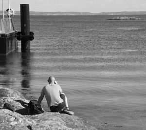 Rear view on man relaxing on rock by sea