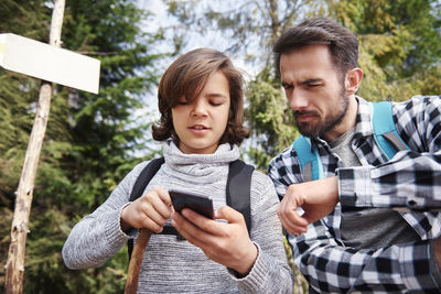 Father and son using mobile phone against trees