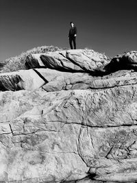 Side view of woman standing on rock against sky