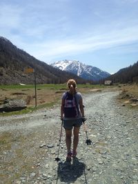 Rear view of hiker walking on dirt road at mountain against sky