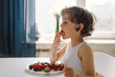 Cute beautiful little boy eating fresh cherry and strawberry.