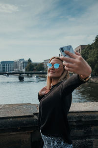 Smiling young woman taking selfie while standing in city