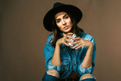 Portrait of beautiful young woman drinking glass against wall