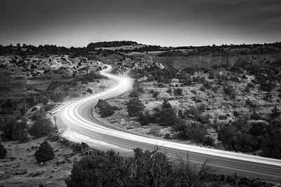 Light trails on road by mountains against clear sky at night