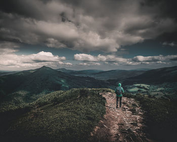 Rear view of mid adult woman walking on mountain against cloudy sky