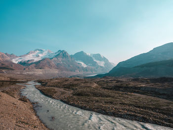 Stream by mountains against clear blue sky