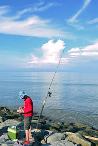 Man fishing by sea against sky