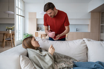 Loving husband holding cup of hot tea made for sick wife having influenza, virus, covid, fever