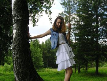 Portrait of smiling young woman standing on tree trunk in park
