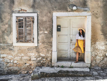 Young woman in summer outfit standing in front of old white wooden door of an old house.