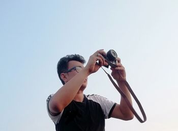 Man photographing with camera against clear sky