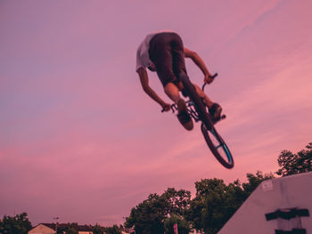 Low angle view of silhouette man jumping on tree against sky