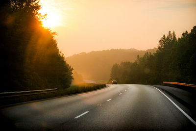 Road amidst trees against sky during sunset