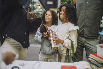 Smiling female siblings looking up while holding toys at flea market