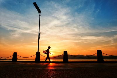 Silhouette man standing on bridge against sky during sunset