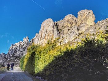 People walking on rock formation against sky