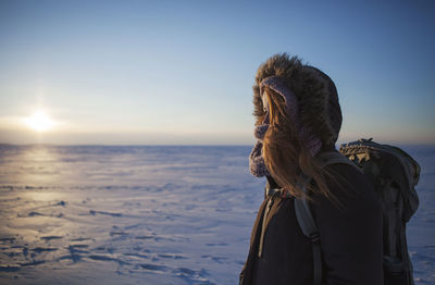 Side view of woman standing on snow covered landscape against sky