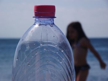 Close-up of water bottle on sea shore against sky