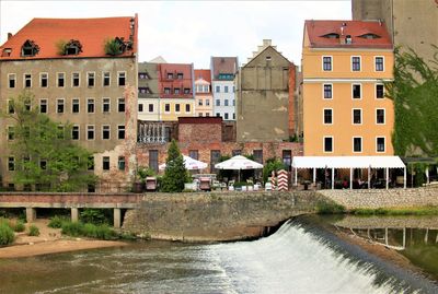 Buildings by river against sky in city