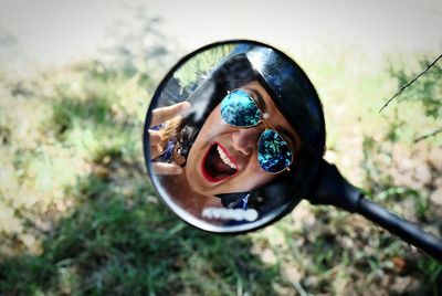 Reflection of woman wearing helmet and sunglasses gesturing horn sign in side-view mirror of motorcycle