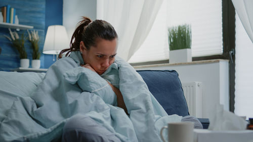 Sick woman wrapped in blanket sitting on sofa