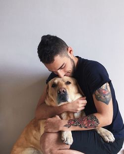 Man embracing dog against wall