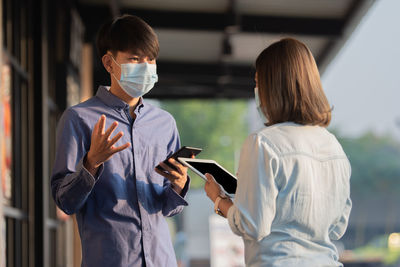 Colleagues wearing mask looking at digital tablet while standing outdoors