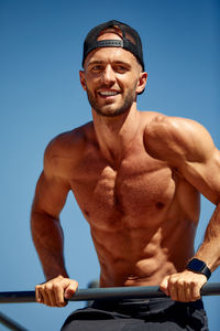 Portrait of shirtless man standing against clear blue sky