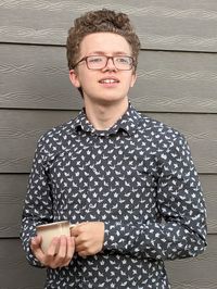 Portrait of teenaged boy wearing eyeglasses and holding a coffee cup standing against wall
