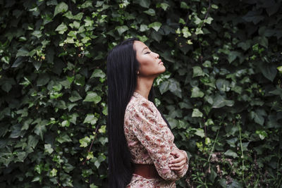 Side view of young woman standing against plants