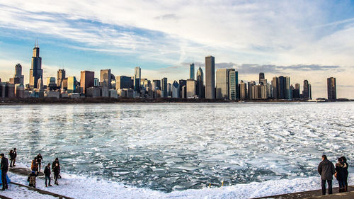 People on city by sea during winter against sky