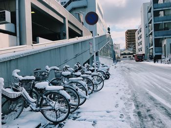 Bicycles parked on snow covered road by buildings in city