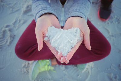 Low section of person holding heart shape on sand