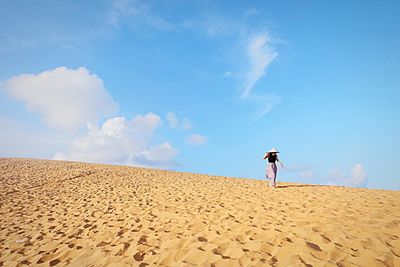 Woman walking on sand dune in desert against sky