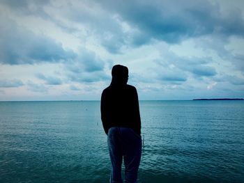 Rear view of silhouette man standing by sea against sky