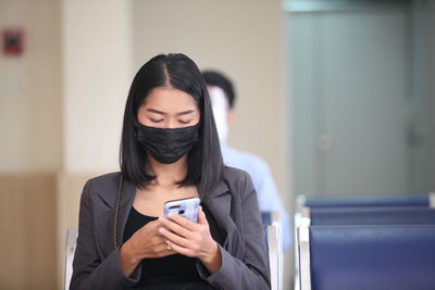 Woman wearing mask using mobile phone while sitting on chair outdoors