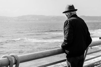 Rear view of man standing by railing against sea