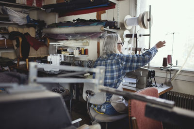 Senior owner using sewing machine at table in workshop