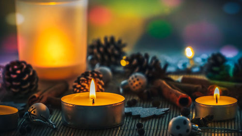 Close-up of burning tea lights amidst pine cones on table