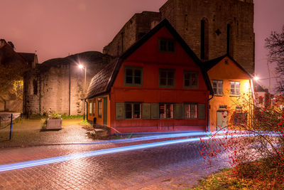 Illuminated buildings by street against sky at night