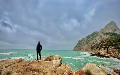 Rear view of man standing on rock by sea against sky