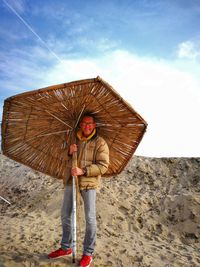 Portrait of smiling man with thatched umbrella standing on beach