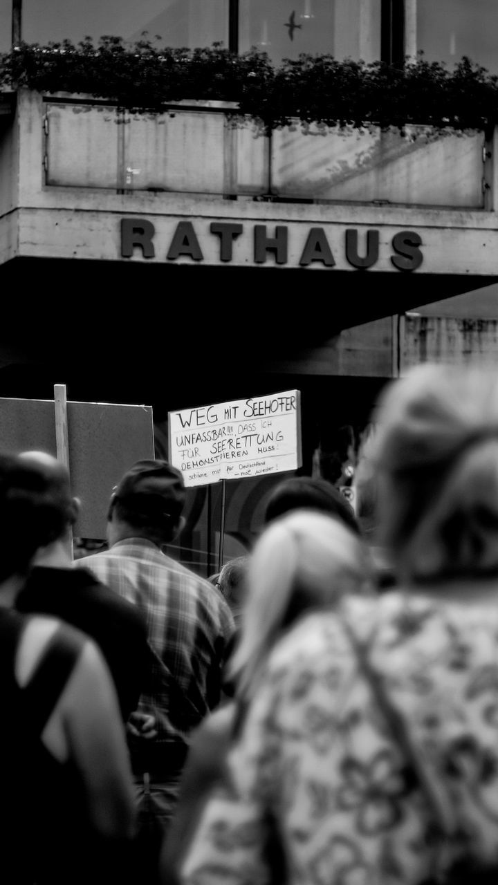 real people, group of people, women, people, selective focus, adult, men, architecture, text, city, lifestyles, built structure, street, communication, leisure activity, crowd, portrait, incidental people, day, focus on background, human face